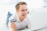 Cheerful casual young man doing online shopping on sofa