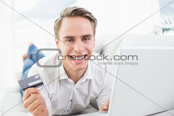 Cheerful casual young man doing online shopping on sofa