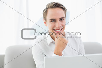 Smiling casual young man using laptop on sofa