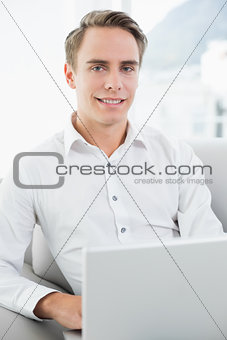 Portrait of a smiling casual young man using laptop on sofa