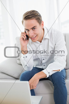Casual young man using cellphone and laptop on sofa