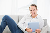 Casual smiling young man using digital tablet on sofa
