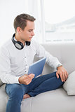 Casual serious young man using digital tablet on sofa