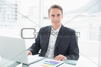 Smiling young businessman with laptop at office desk