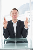 Smiling businessman with fingers crossed at office desk