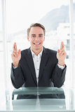 Smiling businessman with fingers crossed at office desk