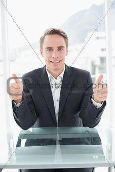 Smiling businessman gesturing thumbs up at office desk