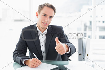 Businessman writing documents and gesturing thumbs up at office desk