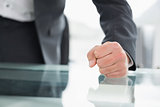 Mid section of businessman with clenched fist on office desk