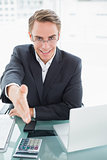 Elegant businessman offering a handshake at office desk