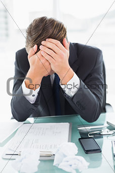 Worried businessman with head in hands at office desk