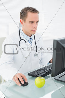 Serious male doctor using computer at medical office