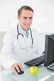 Smiling male doctor using computer at medical office