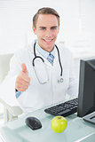 Doctor using computer while gesturing thumbs up at medical office