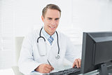 Smiling doctor writing note while using computer at medical office
