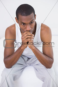 Thoughtful Afro man sitting on bed