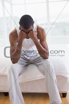 Thoughtful young Afro man sitting on bed