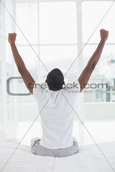 Afro man waking up in bed and stretching his arms