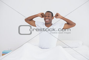 Afro man waking up in bed and stretching his arms