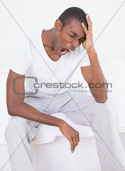 Young Afro man yawning in bed at home