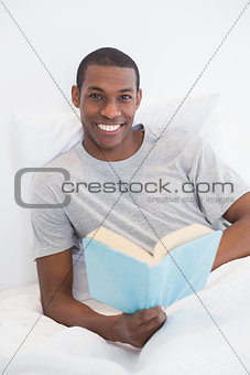 Smiling young Afro man with a book in bed