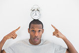 Close up portrait of a man pointing at alarm clock over his head