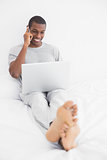 Afro man using cellphone and laptop in bed