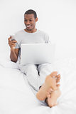 Afro man text messaging while using laptop in bed