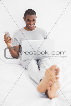 Afro man text messaging while using laptop in bed