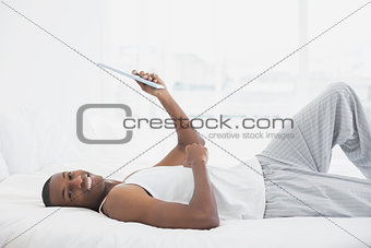 Smiling Afro man resting with digital tablet in bed
