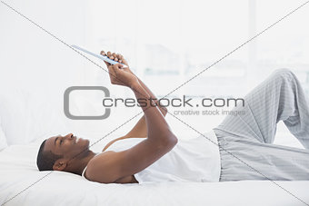 Side view of smiling Afro man using digital tablet in bed