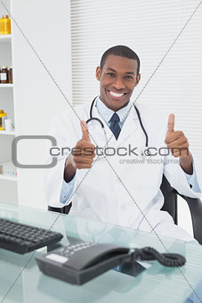 Doctor with computer while gesturing thumbs up at medical office