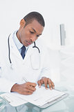 Serious male doctor writing a note