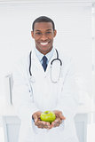 Smiling doctor holding a green apple at medical office