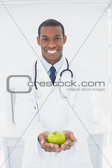 Smiling doctor holding a green apple at medical office