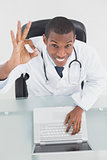 Overhead of a smiling male doctor with laptop gesturing okay sign