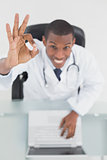 Overhead of a smiling doctor with laptop gesturing okay sign