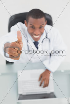 Smiling male doctor with laptop gesturing thumbs up