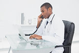 Male doctor using phone and laptop at medical office