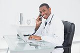 Smiling doctor using phone and laptop at medical office