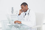 Doctor using cellphone and laptop at medical office
