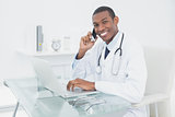 Smiling male doctor using cellphone and laptop