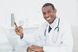 Smiling male doctor text messaging while using laptop