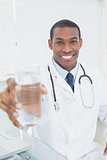 Smiling doctor holding out a glass of water in medical office