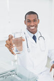 Male doctor holding out a glass of water in medical office