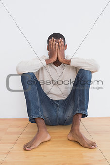 Man sitting against wall with hands covering face