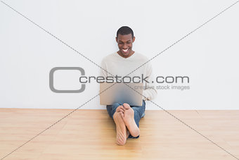 Casual Afro man using laptop on floor in an empty room