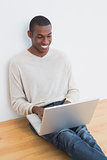 Happy casual Afro young man using laptop on floor