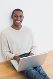 Happy casual Afro young man using laptop on floor