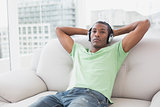 Relaxed Afro man with headphones sitting on sofa in house